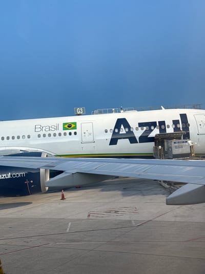 An Azul Linhas Aéreas Brasileiras aircraft is prominently featured in this daytime image, parked on an airport tarmac under a clear blue sky. The photo is taken from a slightly elevated perspective, looking towards the side of the airplane.
The main subject is the white fuselage of the aircraft, emblazoned with the large, dark blue "Azul" logo. Below the cockpit windows, a small sign marked "G3" indicates the gate number. Further along the fuselage, the word "Brasil" is written in black, accompanied by a vibrant Brazilian flag. The aircraft's wing extends into the frame, partially obscuring the view of the ground and the far side of the plane. One of the aircraft's engines is visible below the wing, bearing the "azul.com" web address.
The aircraft appears to be undergoing servicing or preparation. A cargo container, labeled "RKN 01621 XK," is positioned near an open cargo door on the fuselage, suggesting cargo loading or unloading is in progress. Parts of a jet bridge or ground support equipment are visible connecting to the aircraft.
The setting is an airport tarmac, with concrete ground marked by white and red lines, indicating designated areas. An orange traffic cone stands on the tarmac near the wing. The weather is clear and sunny, indicated by the bright, cloudless blue sky. No people are clearly visible in the image. Given the provided context, the scene is set at Fort Lauderdale, United States.