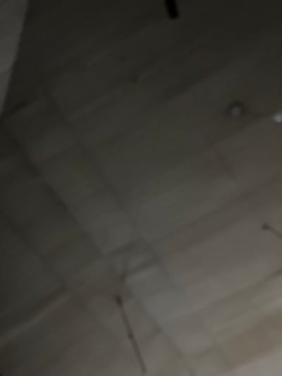 I cannot identify a location in Abeokuta, Nigeria from the image. The image shows a blurry, low-lit, indoor space with what appears to be a ceiling or wall composed of rectangular panels or boards. There are a few dark spots or objects attached to the surface.