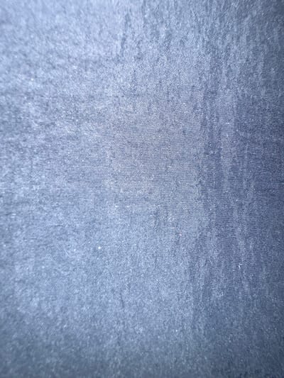 The image displays a close-up view of blue fabric with a textured weave, likely denim or a similar material. The lighting creates a slightly gradient effect, with the top left appearing brighter and the bottom right darker. The fabric exhibits a subtle pattern of horizontal and vertical threads. There are no identifiable features of Letterkenny, Ireland, or any people or actions present in the image.