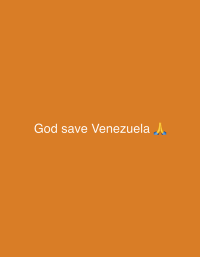 The image is a photograph with a solid orange background. White text is overlaid on the image, reading "God save Venezuela". To the right of the text, there is an emoji of two hands clasped together, resembling a prayer or a gesture of thanks. The text and emoji are centered horizontally and positioned in the lower half of the frame. There are no other discernible subjects, objects, or scene elements. The lighting appears even, suggesting the photo was taken indoors or under uniform lighting conditions, and there are no cues to indicate a specific time of day or weather. No location cues are present in the image itself, and the provided location context of "Pakhtakor, Uzbekistan" is not visually supported by the image content. The overall emotion conveyed is one of hope, plea, or devotion, as suggested by the text and the prayer emoji.
