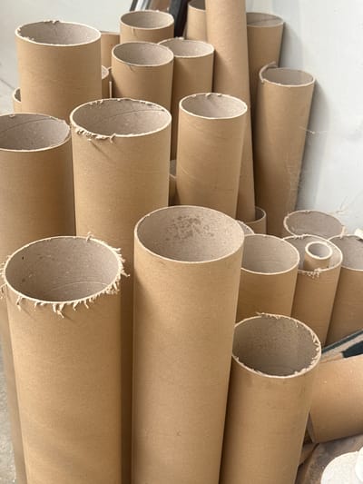The image shows a collection of cardboard tubes, likely used as cores for paper or other rolled materials. They are standing upright, in various sizes and heights, and are arranged in a dense grouping against a plain, light-colored wall. Some of the tubes are partially visible, suggesting they are stored in a warehouse or workshop. The lighting is even, and there are no people or other discernible objects in the scene. The location is not specified in the image itself, and thus, its presence in the city of Fontevivo, Italy cannot be confirmed.
