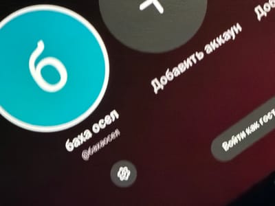 The image displays a close-up of a digital interface, likely on a screen, featuring several elements. A large teal circle prominently displays a white number "6." To the right of this circle, a dark gray circular icon contains a white plus sign. Further to the right, white text is visible in a curved orientation, with the first word appearing to be "Добавить" (Add). Below this, more white text reads "аккаунт" (account). To the left of the "6," white text reads "баха орел," and below it, a username is partially visible, "@bax20cer." A small, circular icon resembling a gear or cogwheel is positioned below the username. In the lower right portion of the image, a white bar with rounded ends contains white text that reads "Войти как гост" (Log in as a guest). The background of the image is a dark, mottled color, with a reddish hue in some areas, suggesting a screen display. There are no people or any indication of a specific city, let alone Avdarma, Moldova, within the image itself.