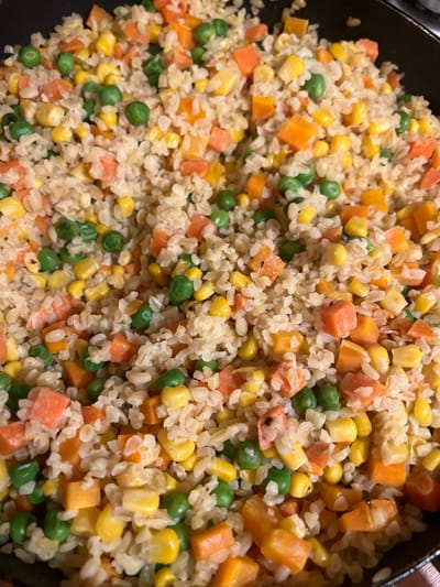 A close-up, overhead shot shows a pan filled with a mixture of rice, peas, corn, and diced carrots. The food appears to be cooked and is a common side dish or a simple meal. There are no people or any other discernible objects in the frame other than the food and the pan it is in. There is no information in the image that can be used to determine the location in Skawina, Poland.