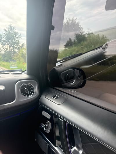 The image shows the interior of a car, specifically the dashboard and part of the door. The car is parked, with the view outside the window showing trees and the sky. The air vents and some control buttons are visible on the dashboard. The door features leather upholstery with diamond stitching. The image does not provide any information regarding the location in the city of Bazan, Bulgaria.