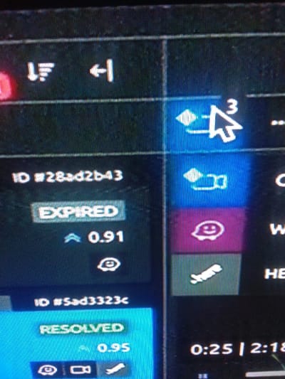 This image is a photograph of a digital screen, depicting a user interface within an unspecified indoor environment in Mista Ali, Nigeria. The screen displays a dark background with various illuminated white, grey, blue, pink/magenta, and green graphical elements and text.
In the upper-left, a row of three white icons is visible: a 'sort' or 'filter' icon (three horizontal lines with a down arrow), a 'back' or 'return' arrow icon, and a partially obscured third icon. To the right of these, a white mouse cursor is positioned over a glowing blue icon. This icon features a diamond shape connected to a right-pointing arrow, with a white superscript numeral '3' near the arrow's head. Below this, another similar blue icon (diamond with a right-pointing arrow) is present.
The left-middle section of the screen displays white text "ID #28ad2b43". Directly below this, a grey rectangular button shows white text "EXPIRED". Below "EXPIRED", an upward-pointing arrow icon precedes the numerical value "0.91". Further down, a circular icon with an eye symbol is visible.
Adjacent to the "EXPIRED" section on the right, two vertically stacked square buttons are present. The upper button is pink/magenta and contains a white smiley face icon. The lower button is dark green and features a white icon resembling a curved, elongated shape.
In the lower-left section, white text "ID #5ad3323c" is displayed. Beneath it, a blue rectangular button shows white text "RESOLVED". Below "RESOLVED", an upward-pointing arrow icon is followed by the numerical value "0.95". Below this, a row of three small white icons includes an eye symbol, a video camera, and a curved, elongated shape.
In the bottom-right corner, partially visible white text "0:25 | 2:18" suggests a time duration display. The image exhibits pixelation and slight moiré patterns, characteristic of a photograph taken of an active display screen.