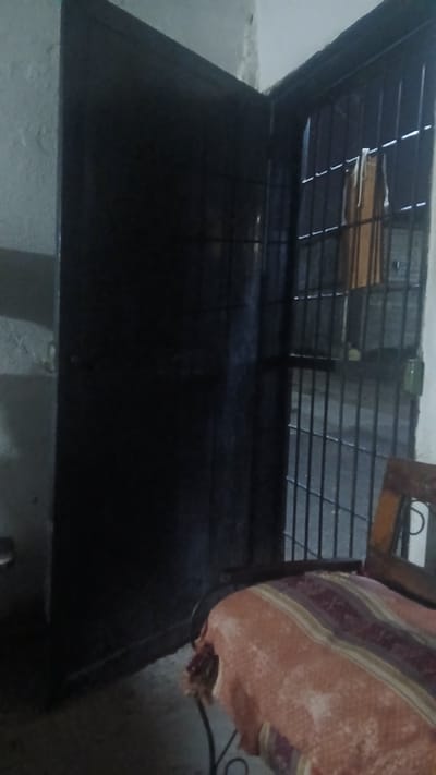 The image shows a metal bed frame with a grated headboard. A folded blanket rests on the right side of the bed. The bed frame appears to be in a room with concrete walls. There is no information to confirm that the image was taken in Putucual, Venezuela.
