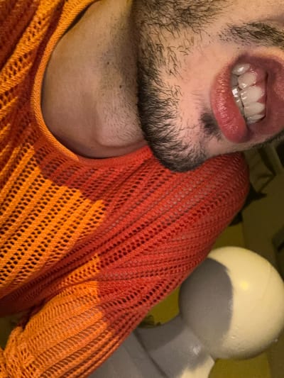 A close-up shot focuses on the lower portion of a person's face, showcasing teeth, lips, and beard. The skin tone appears fair. The person is wearing an orange, loosely knitted or crocheted sweater. In the background, partially visible, is a white, rounded object that appears to be made of plastic. The image provides insufficient information to determine a location in Los Palacios, Spain.
