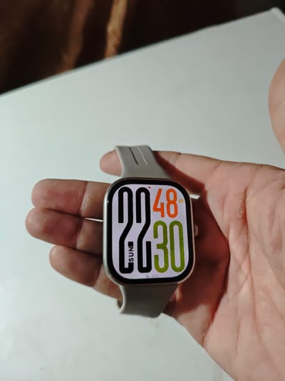 A close-up shot shows a person's hand holding a smartwatch with a digital display. The watch face shows the time "09:48" and "30". The background is blurred, with a white surface in the foreground and a darker, textured surface in the background. The image is not geotagged to Akhmetovskaya, Russia.