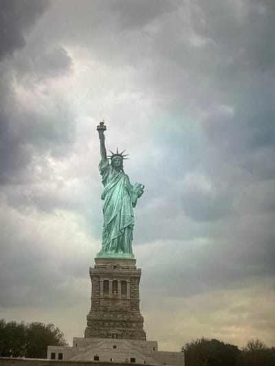 The image shows the Statue of Liberty under a cloudy sky. The statue is on its pedestal. The location is not in Des Plaines, United States, but in New York City.