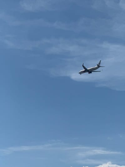 An airplane is captured in mid-flight against a clear blue sky with wispy clouds. The aircraft is white with red accents on its engines and tail. It appears to be a commercial airliner, possibly on approach or departure from an airport. The image was taken near Villeneuve-le-Roi, France, a commune located in the Val-de-Marne department, southeast of Paris.
