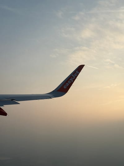 The image features the tail of an EasyJet airplane against a backdrop of a cloudy, textured sky. The tail fin is red with the "easyJet" logo in white. The location is difficult to determine definitively from the image alone. While the prompt asks for a location in Peschiera Borromeo, Italy, nothing in the image inherently indicates this specific location.