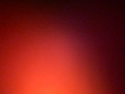 The image displays a gradient of color shifting from dark maroon to a vivid orange. The maroon dominates the upper portion, gradually lightening into shades of red before transforming into the bright orange at the bottom. The texture has a grainy appearance throughout the entire image.