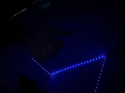 A dark, angled image captures a hand silhouetted against a surface lit by a string of blue LED lights. The lights form a zig-zag pattern, accentuating the edges of what appears to be a box or structure. The background is predominantly black, with the blue light reflecting slightly off the surface. The overall impression is one of low-light conditions with artificial illumination creating a distinct visual effect. The location in Ludwigshafen am Rhein, Germany is not discernible from the image.