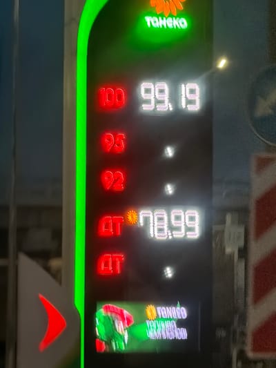 This media file shows a close-up, nighttime, vertical shot of a digital display board. The display shows several numbers and text, illuminated by LED lights. On the left, a green floral design with green text that appears to read "TONOBO". To the right of this, two columns of numbers are displayed in white. The left column shows "99.19" and below it "100". The right column shows "66.89" and below it "92". To the far right, there is an image of a red and green cartoon figure, possibly Santa Claus, and text that appears to read "TONGEIO GEOTONTIADO".
Below the white numbers, there are two columns of red numbers. The left column shows "92" and below it "52". The right column shows "78" and below it "70".
The scene is indoors or in a sheltered area, given the clarity of the display and the lack of discernible outdoor elements. The lighting suggests it is nighttime, or that the display is in a dim environment. The context provided, Zhilino-1, Russia, is noted. The overall impression is that of a commercial display, perhaps for prices, promotions, or information. There is a distinct green neon-like band running horizontally across the lower portion of the visible display.