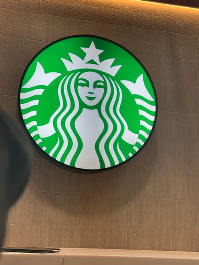 The image shows a Starbucks logo mounted on a wall. The logo is green and white, featuring the iconic Siren. The wall has a textured, tan surface resembling tiles. The photograph appears to be taken indoors. There is no visible evidence indicating the location of the city of Pudahuel, Chile.