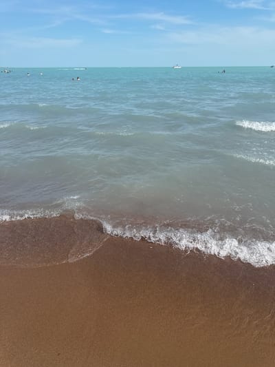 This media file depicts a serene beach scene with the clear blue sky transitioning to the gentle waves of the ocean. The scene is divided into two distinct parts: the left side showcases the vast expanse of the sky with a few scattered clouds, while the right side presents the calm ocean meeting a sandy beach.
Several individuals are visible in the water, enjoying a leisurely day at the beach. Some are swimming, while others appear to be standing or wading. A white boat is also present in the distance, adding to the maritime ambiance. The waves are small and lapping, creating a tranquil and inviting atmosphere. The sandy shore is a warm brown, contrasting with the cool blue hues of the water and sky.
The time of day appears to be daytime, with the sun casting a gentle light on the scene. The weather seems pleasant, suitable for a beach outing. While no specific textual information is visible, the scene evokes a sense of relaxation and enjoyment. The location context of Shubatubek, Kazakhstan, suggests a coastal area with these characteristics.