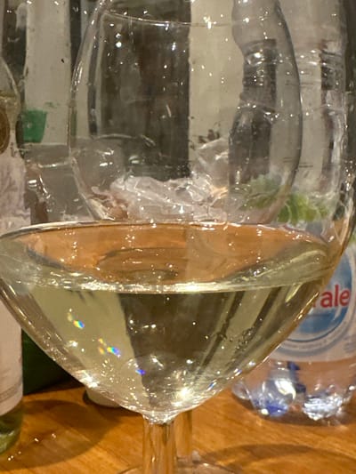 A close-up shot shows two water-filled wine glasses positioned on a wooden surface. A plastic water bottle is visible in the background, labeled with "ale". The scene is brightly lit, emphasizing the transparent nature of the glasses and the water within. It is impossible to confirm the location is Tumbak Bayuh, Indonesia based on the image. There is no mention of people.