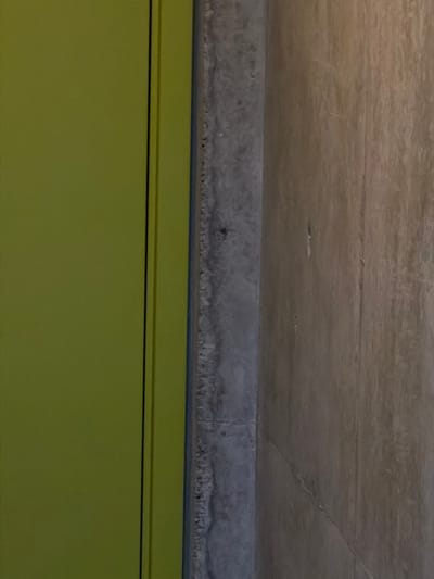 The image shows a section of a building interior in Chkalov, Armenia. A green painted wall is at the bottom of the frame. Above the wall is a horizontal concrete beam or lintel with a rough texture. Above the beam is a concrete ceiling, exhibiting cracks and imperfections. There are no people visible.