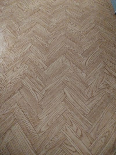 The image shows a close-up, high-angle view of a light-colored, wood-patterned floor laid in a herringbone pattern. The floor is the primary subject of the image, with no people or other objects visible. The scene appears to be indoors, with the lighting suggesting ambient room light. The image does not contain information about the city of Gorodische, Russia, or any specific location within it. The description of the image is purely based on the visual elements present.