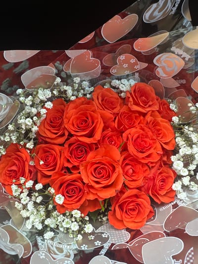 This media file features a close-up, overhead shot of a vibrant bouquet of orange roses, artfully arranged with delicate white baby's breath. The roses, in various stages of bloom, showcase rich, saturated orange petals with a soft, velvety texture. The accompanying baby's breath provides a lovely contrast with its small, star-shaped white flowers and airy green stems.
The bouquet is partially wrapped in clear cellophane that is decorated with an array of heart shapes in shades of pink, orange, and white. Some of the hearts have subtle patterns, while others are solid. Faintly visible text, likely in French, appears on some of the hearts, including "l'amour" and "l'iel". The background appears to be a dark, solid surface on the left side of the frame, possibly a table or a piece of fabric. The overall presentation suggests a gift or a decorative arrangement, perhaps for a special occasion like Valentine's Day or an anniversary. There are no people or animals visible in the image. The lighting is bright and even, highlighting the rich colors of the flowers. The context of Bad Endorf, Germany, does not provide specific visual cues within the image itself.