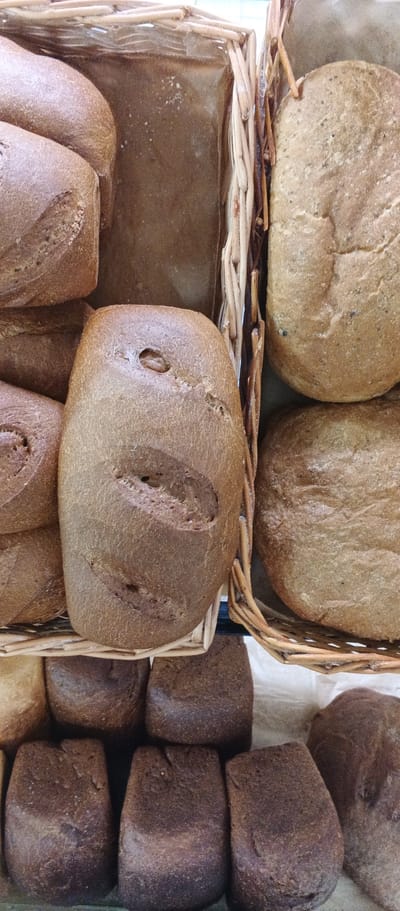 The image depicts an assortment of rustic loaves of bread displayed in wicker baskets and on a surface. The breads vary in size and shape, with some being round and others rectangular. Their crusts are a rich brown color, some appearing cracked or scored. The setting appears to be a market or bakery, given the presentation of the baked goods. There are no people or animals visible in the image. The image does not contain any information that would allow for determination of its location in the city of Ploske, Ukraine.