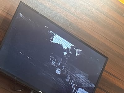 A television, an LG brand, sits on a wooden surface. The screen displays an image from a camera located on a street in Eneka, Nigeria. Multiple cars are on the street. Houses are visible along the street.