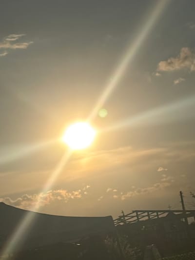 The image depicts a bright, overexposed sky with the sun prominently visible, producing strong lens flares. There are faint clouds scattered throughout the sky. In the lower right corner, a dark silhouette of a building or structure is present. In the upper right corner, there's a power or telecommunication pole, which indicates the location of the urban environment. There is no information in the image that shows that this scene is in Kukorevo, Bulgaria.