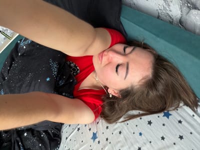 The image shows a person lying on a bed, seemingly taking a selfie. The person is wearing a red shirt and has brown hair. The bedsheets are patterned with stars. The background appears to be a wall with textured wallpaper. The scene is indoors and appears to be a bedroom. There is no indication of the city of Старые Туймазы, Russia, or any specific location within it.
