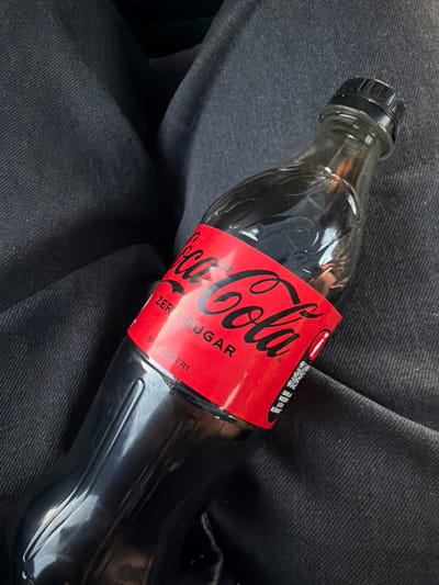 The image shows a Coca-Cola Zero Sugar bottle resting on dark denim fabric. The bottle has a red label with the Coca-Cola logo and the words "ZERO SUGAR" and "SOCKERFRI". The scene is indoors, and there are no discernible city landmarks or specific locations in Munkedal, Sweden.