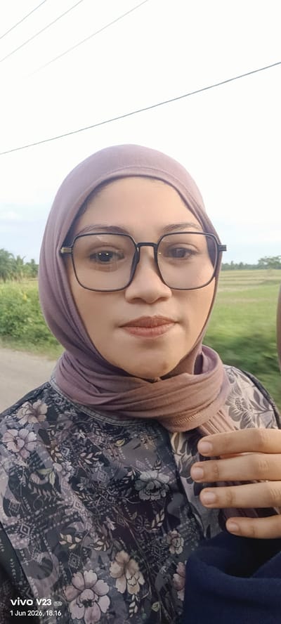 A person wearing a hijab and glasses is posing for a selfie outdoors. The person is wearing a floral patterned shirt. In the background, a field and some trees are visible. Overhead power lines are in the top left corner. The location is Matangsijuek Timur, Indonesia, as indicated by the date and time stamp. The date and time are June 1, 2026, 18:16. A hand with fingernails is visible in the lower right.