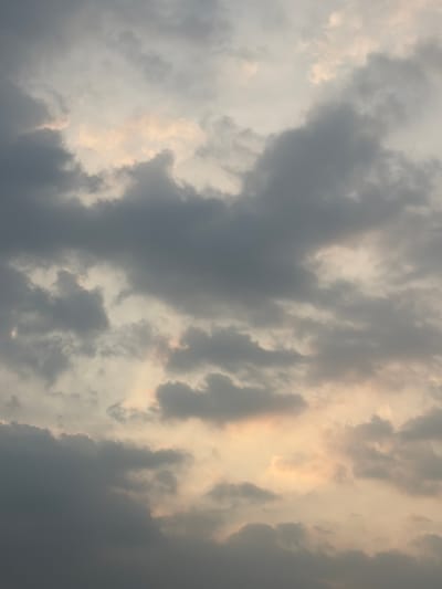 This is a vertical, medium shot of a cloudy sky, likely taken during the daytime. The clouds are varied in color and density, ranging from dark gray to light white, with some areas illuminated by sunlight, creating a warm, golden glow. The light filtering through the clouds suggests it might be late afternoon or early evening, or a moment when the sun is breaking through an overcast sky. There are no people or man-made objects visible. The scene evokes a sense of natural beauty and perhaps a hint of dramatic weather. There is no visible text in the image. The location context provided is Denasri Kulon, Indonesia, which does not offer specific visual cues within the image itself.