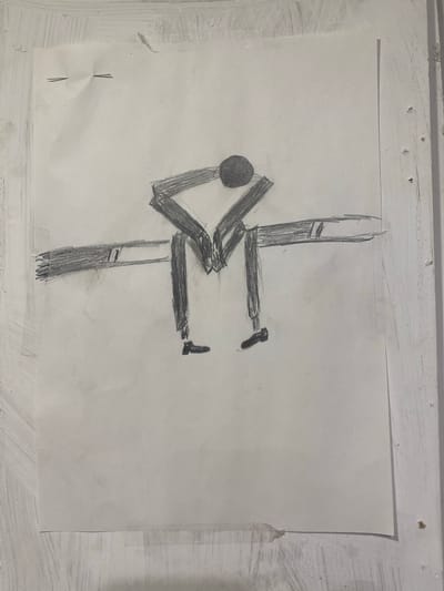 The image displays a simple pencil drawing on a sheet of paper. The drawing depicts a stylized human figure with a round head, bent over with its arms wrapped around its knees. The figure appears to be sitting on a horizontal bar or bench, with its legs dangling. The drawing is rendered in a basic, somewhat abstract style, with thick lines and minimal detail. The paper itself shows signs of being attached to a surface, with two staples visible at the top left corner. The background is a light, textured surface that appears to be a wall. There is no information within the image that suggests a specific location in Legenda, Egypt.