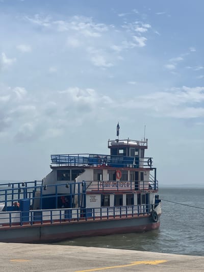 A ferry, identified by the text "FERRY OMETEPE N° 1" on its side, is docked at a concrete pier. The ferry is a multi-level vessel with a white and blue exterior. It has multiple windows, railings, and life preservers visible. A dark flag is flying from a pole on the top deck. The water is choppy, and the sky is partly cloudy. The location appears to be a port in Moyogalpa, Nicaragua, as suggested by the ferry's name referencing Ometepe Island, a prominent feature of Lake Nicaragua near Moyogalpa. There are no people clearly visible in the image.