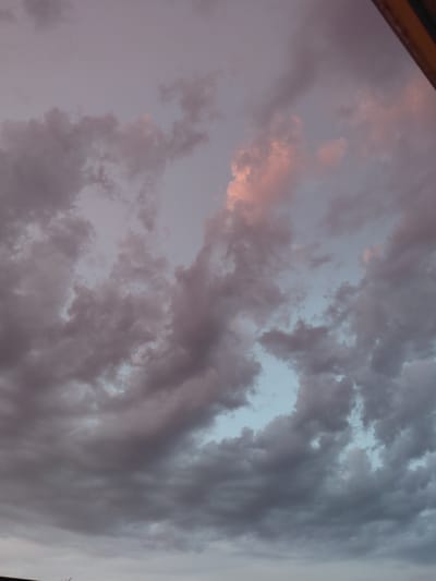 This image shows a cloudy sky with muted colors, possibly during twilight or a very overcast day. The clouds are dark gray and purplish, with hints of pink and light blue peeking through in some areas. The scene is an exterior shot, focusing solely on the sky. There are no people, subjects, objects, or actions visible in the image. The composition is abstract, emphasizing the texture and color of the clouds. The image does not contain enough information to determine its specific location in Ecublens, Switzerland.