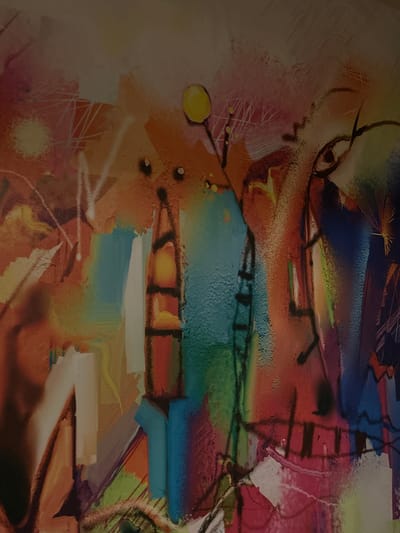 The media file displays a vibrant and complex abstract painting, rich in color and dynamic composition. The artwork features a striking interplay of warm hues like reds, oranges, and yellows, contrasting with cool tones of blues, greens, and purples. Bold black lines and outlines are prominent throughout, defining various abstract shapes and creating a sense of depth and movement.

On the left side of the composition, a subtly suggested, abstract face or profile can be discerned. It includes an eye with a distinct pupil and brow, rendered with lighter tones and brushstrokes that imply texture or hair. Scattered around this area are small, round yellow elements.

The rest of the canvas is filled with an energetic mix of layered forms. These include geometric shapes such as rectangles and irregular blocks, alongside more organic blobs and intricate linear patterns. Some areas exhibit a grainy, spray-painted texture, while others show smooth color applications or visible brushstrokes, suggesting a mixed-media approach. Ladder-like structures formed by black lines appear on the right side, further contributing to the artwork's complexity. The overall impression is one of intense visual activity and layering.

No discernible real-world objects or legible text are present within the artwork, which showcases a purely abstract expression. The image itself appears to be a photograph of the artwork, taken in what seems to be a slightly dim lighting condition. The location context of Esenler, Turkey, does not provide specific visual cues within the artwork itself.