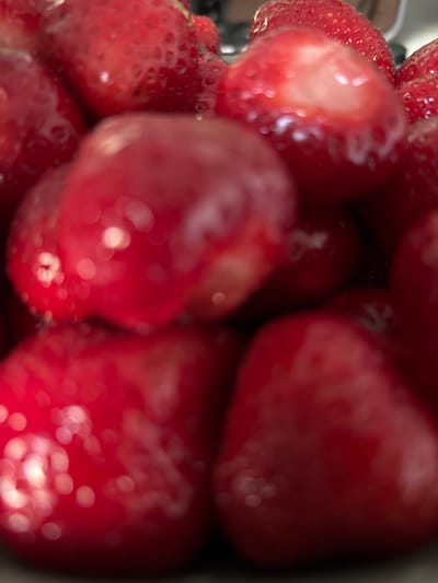 A close-up, out-of-focus photograph shows a pile of bright red strawberries. The lighting creates specular highlights that appear as circles of white light on the surface of the fruit. The image is a still life and does not contain any information about its location in Mülheim an der Ruhr, Germany, nor does it depict any people or actions.