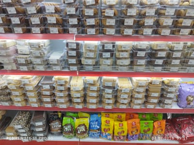 The image shows a retail display of confectionery products in a store. The products are arranged on shelves, with rows of plastic-wrapped cookies and candies. The items include various types of cookies in clear plastic containers and bagged candies in colorful packaging. Some of the packaging features text and logos, including "Pure Love," "Candy Gold," and "Yamelly." A timestamp and text "REDMI NOTE 11 PRO 5G" are visible in the lower portion of the image. The scene appears to be indoors, in a well-lit environment, likely a supermarket or a dedicated candy store. Based on the metadata, the image was taken in Navrouz, Uzbekistan on July 4, 2026, at 09:51.