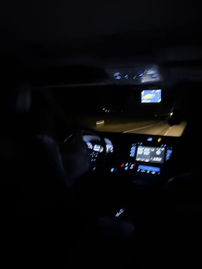 The image depicts the interior of a vehicle at night. The dashboard and steering wheel are visible, illuminated by the faint glow of the instrument panel and infotainment screen. The environment is dark, with little to no ambient light. The location in the city of Kuchak, Armenia is not discernible from the image.