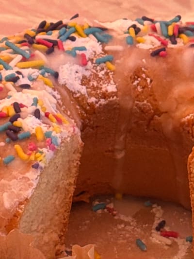 The image depicts a donut with colorful sprinkles and icing. A portion of the donut appears to be cut out, revealing the interior. There is no indication of location in Fentange, Luxembourg, people, or specific actions/interactions within the frame. The focus is solely on the donut.