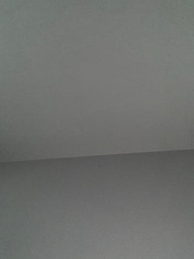 The image displays a grey, textured surface, characterized by a fine, granular texture suggestive of concrete or a similarly finished wall. A subtle, relatively straight horizontal line divides the frame into two distinct planes: an upper section and a lower section. The upper section exhibits a slightly lighter shade of grey compared to the lower section, indicating a difference in lighting, angle, or surface property. The overall scene is devoid of any specific objects, people, or discernible actions. The environment depicted is an interior or exterior wall surface, located in the city of Sauðárkrókur, Iceland.