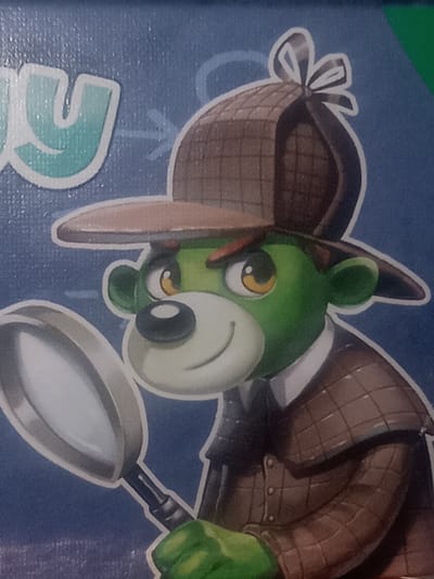 The image is a close-up of a cartoon character depicted as a green ape wearing a detective's deerstalker hat and a plaid coat. The character is holding a magnifying glass. The background is a blue gradient with some white graphic elements that appear to be part of a larger design or text. There is no discernible indication of the city of Kielce, Poland, or any other specific geographical location within the provided image. The image focuses solely on the illustrated character and its immediate surroundings within the artwork.