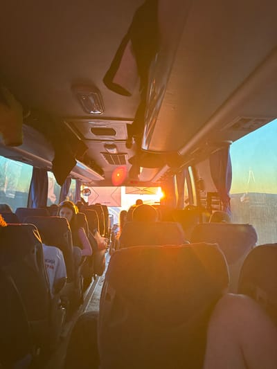 The image depicts the interior of a bus, likely traveling during sunrise or sunset, based on the golden light. Passengers are seated in rows, with their belongings stowed around them. Text in Cyrillic is visible on a bag. A label with "HIGER" can be seen near the windshield. The precise location in Ustinovo, Russia cannot be determined from this image alone.
