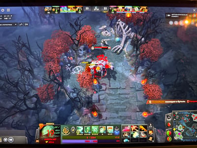 This is a screenshot of a video game, likely Dota 2, captured from a computer monitor. The game's interface, including player statistics, abilities, and a minimap, is visible. The game appears to be set in a dark, mystical forest environment with red foliage and stone pathways.
The image does not contain any information about the city of Wervik, Belgium.