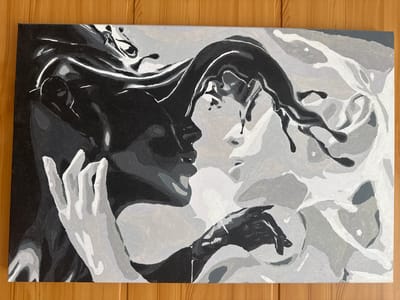 This is a photograph of a monochromatic acrylic painting on canvas, depicting a close-up of two figures in an embrace. The figures are rendered in shades of black, white, and gray, suggesting a dramatic and passionate interaction. One figure, on the left, has dark hair and a pale hand reaching out, with defined fingers. The other figure, on the right, appears to have lighter hair and a face that is partially obscured, with another hand reaching towards the center of the composition. The overall style is abstract, with bold brushstrokes and distinct areas of color defining the forms. The painting is displayed horizontally and is positioned on a wooden surface, likely a table or floor, with visible wood grain. The context of the city of Vurnary, Russia, is not present in the visual information of the image.