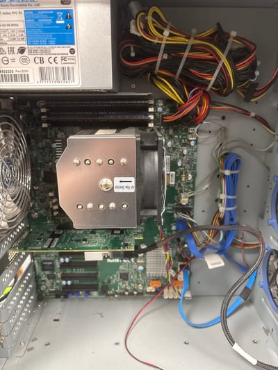 The image shows the inside of a computer case, likely a desktop PC. The main components visible are the motherboard, a CPU cooler with a fan, various cables (including power and data cables), and a power supply unit. The components are housed within a metal chassis. There are no people or animals in the image. The environment is the interior of a computer. There is no information in the image that can be used to determine the location in Mülheim an der Ruhr, Germany.