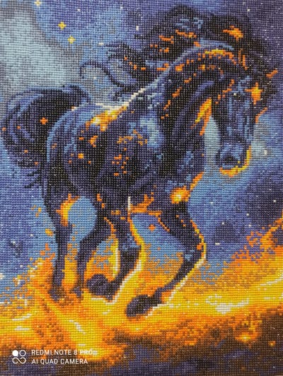 The image depicts a close-up of a diamond painting featuring a dark horse engulfed in flames against a starry night sky. The horse is depicted in motion, with its mane and tail flowing. The flames are rendered in bright oranges, yellows, and reds, creating a stark contrast with the deep blues and purples of the background, which is dotted with white and yellow "stars". The diamond painting technique results in a textured, mosaic-like appearance. The bottom left corner of the image contains a watermark that reads "REDMI NOTE 8 PRO AI QUAD CAMERA". There is no indication of any specific location in the city of Kugesi, Russia within the image itself or its content.