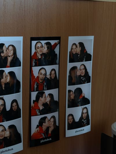 The image shows three photobooth strips lying on a wooden surface. Each strip contains four images of two young women. The women are embracing and kissing in various poses. The strips are labeled "photobox." The image does not show the city of Shul'gino, Russia, or provide any information to suggest that it was taken there.