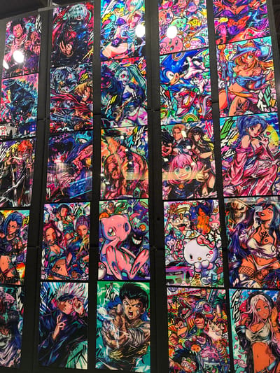 The image displays a wall covered with numerous vibrant, colorful, anime-style artwork panels. The panels are arranged in a grid-like fashion, with multiple columns and rows. Each panel features distinct characters and scenes, rendered in a highly detailed and stylized manner. The artwork appears to be for sale or exhibition, possibly at a convention or market. The overall aesthetic is energetic and visually stimulating, with a focus on popular anime characters and themes. The location of this display is at the Paris-Nord Villepinte Exhibition Centre in Villepinte, France.