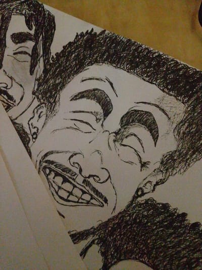 The image is a close-up, overhead shot of a pen and ink drawing on white paper. The drawing features multiple faces in profile, overlapping and layered. The central and most prominent face is laughing with its eyes closed and mouth wide open, revealing teeth and a mustache. To the left, another face is partially visible, also with its eyes closed. A third face, in the lower right quadrant, is depicted with curly hair and an open mouth. The drawing style is characterized by bold, expressive lines and heavy cross-hatching for shading, particularly on the hair and facial features. The background of the drawing area is white paper, and behind the paper, a mottled brown surface is visible, suggesting the drawing is resting on a table or similar surface. There are no elements in the image that place it in Rumuomasi, Nigeria.