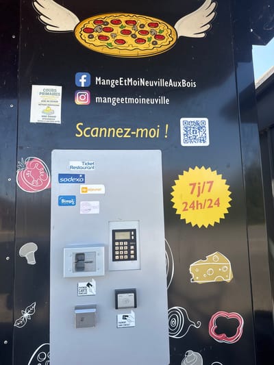This is a close-up shot of a black vending machine, likely for pizza, in Neuville-aux-Bois, France. The left side of the machine is black with a cartoonish pizza graphic featuring mushrooms, pepperoni, and olives. Social media handles for the business “MangeEtMoiNeuvilleAuxBois” are displayed, along with a QR code, the phrase "Scannez-moi!" (Scan me!), and the text "7j/7 24h/24" (7 days/7 24 hours/24), indicating the machine is available around the clock. There is a sticker advertising primary school tutoring services with a phone number and address in Neuville Aux Bois.
The right side of the machine features a gray panel with a number of payment options: a keypad for entering a code, slots and readers for credit cards ("PAIEMENT CARTE BANCAIRE"), contactless payments ("PAIEMENT SANS CONTACT"), and stickers for accepted payment methods like "Ticket Restaurant," "Sodexo," "Up déjeuner," "Edenred," and "Bimpl."
There are several small, cartoonish ingredient graphics on the black background, including a slice of cheese, a red pepper, an onion, and a mushroom.